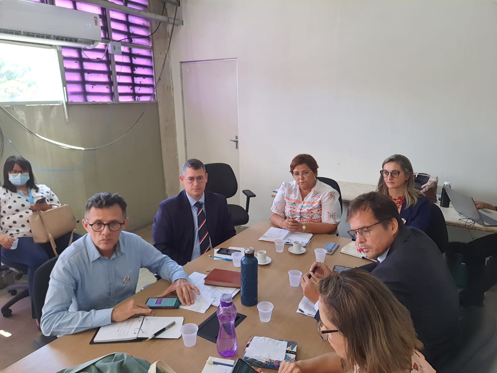 Imagem com várias pessoas sentadas à mesa, realizando uma reunião.