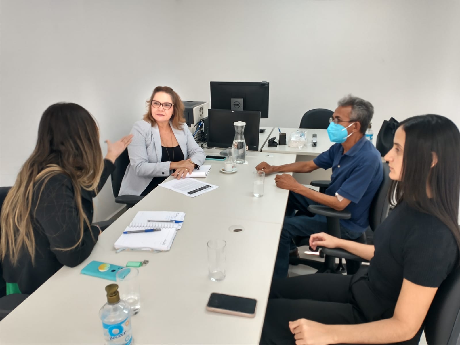 Imagem de uma reunião com três mulheres e um homem, sentados à mesa.