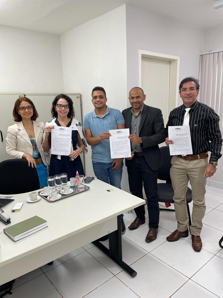 Imagem de duas mulheres e três homens, todos em pé, segurando um documento.