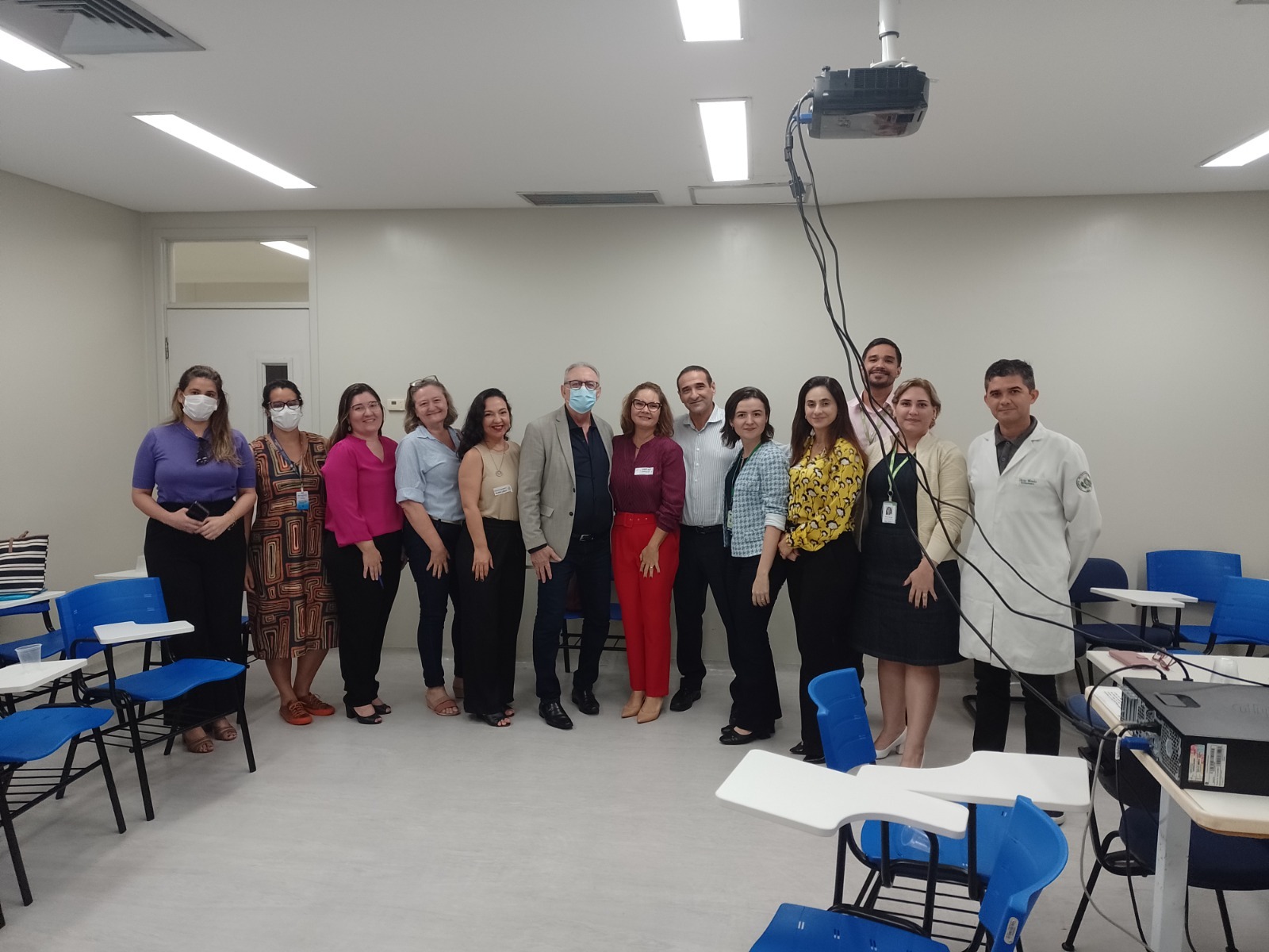 Imagem de 13 pessoas, em pé, uma ao lado da outra, em uma sala, posando para uma foto.