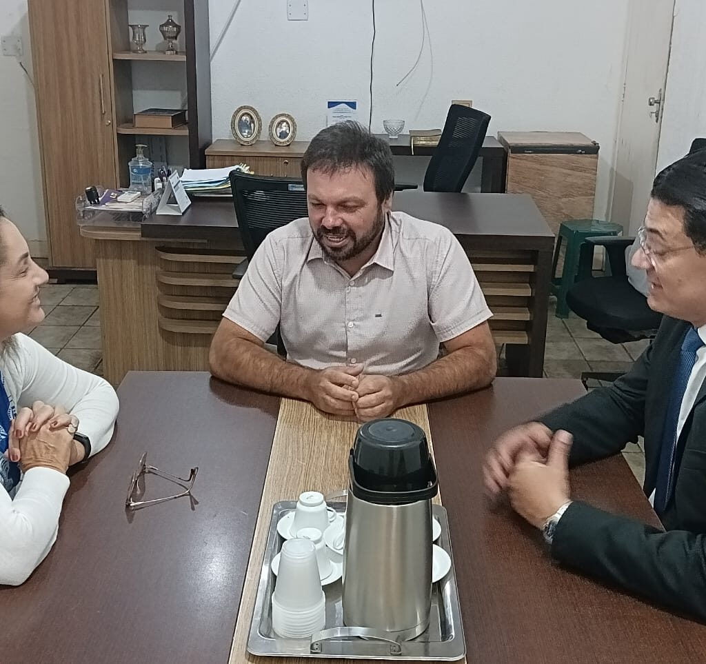 Imagem de dois homens e uma mulher, sentados ao redor de uma mesa, conversando.