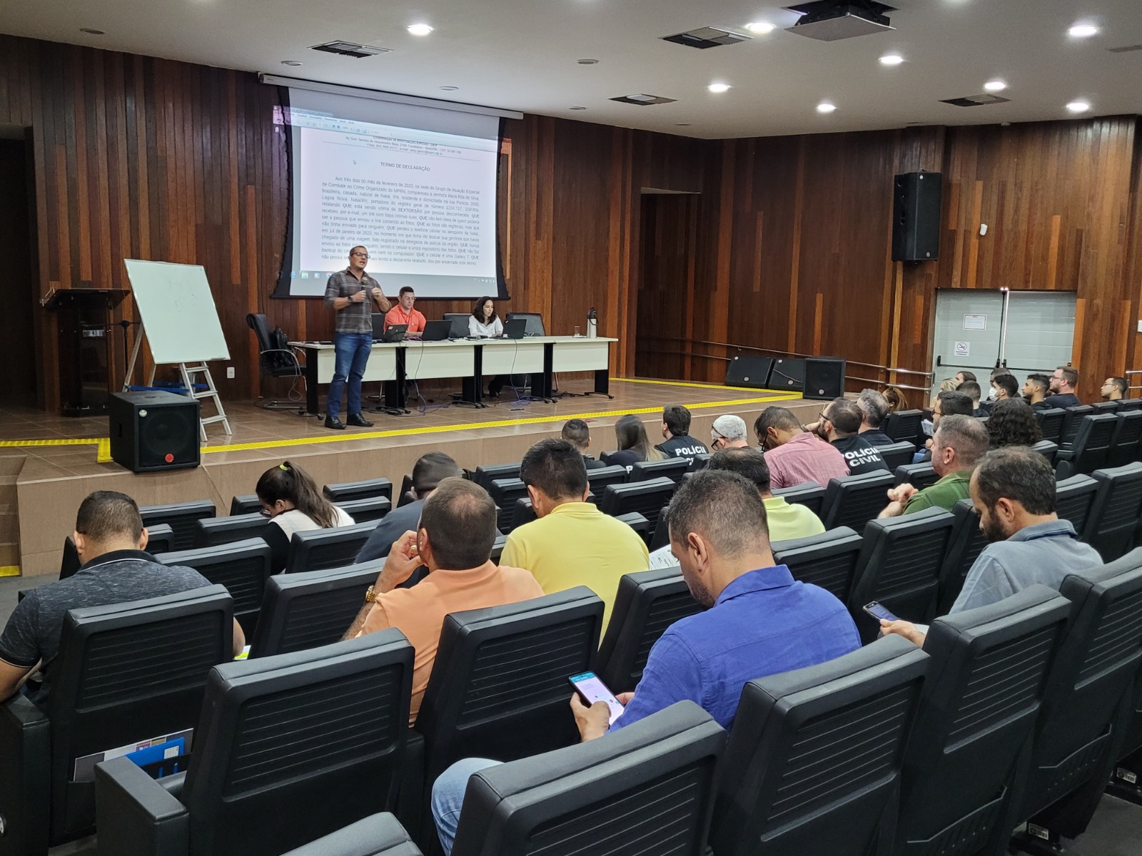Imagem de um auditório com várias pessoas, assistindo a uma palestra.