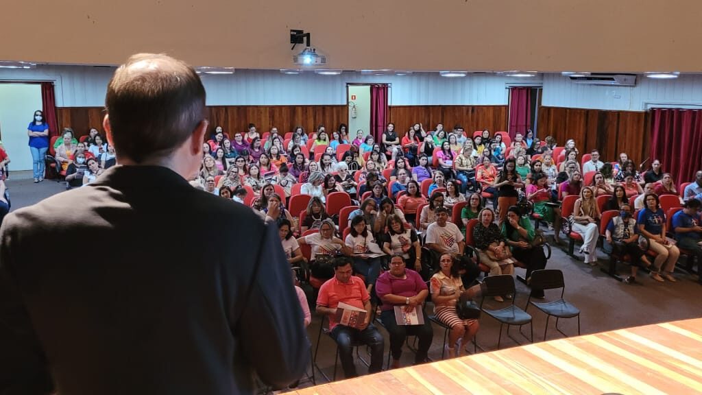 Imagem de um auditório repleto de pessoas e um homem, no palco, falando para essa plateia.