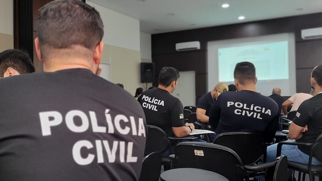 Imagem de policiais sentados, de costas, em um auditório, assistindo a um curso.