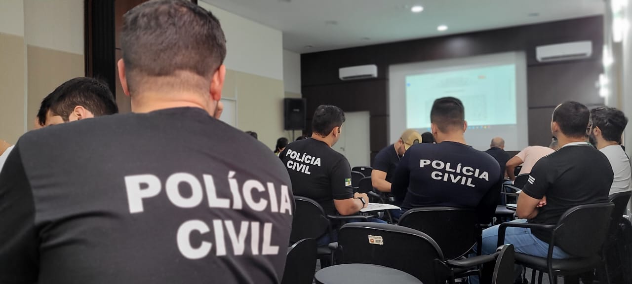 Imagem de policiais sentados, de costas, em um auditório, assistindo a um curso.