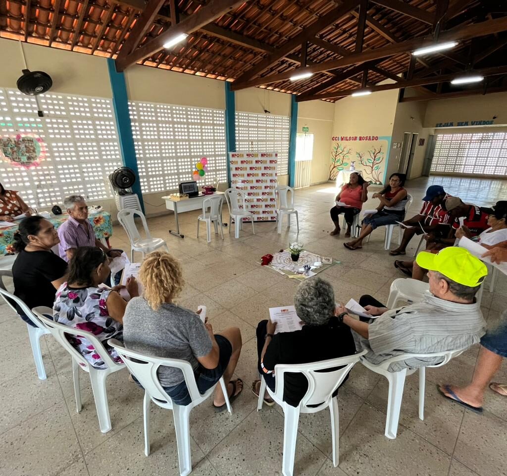 Imagem de várias pessoas idosas sentadas em cadeiras, dispostas em um círculo, durante uma atividade em grupo.