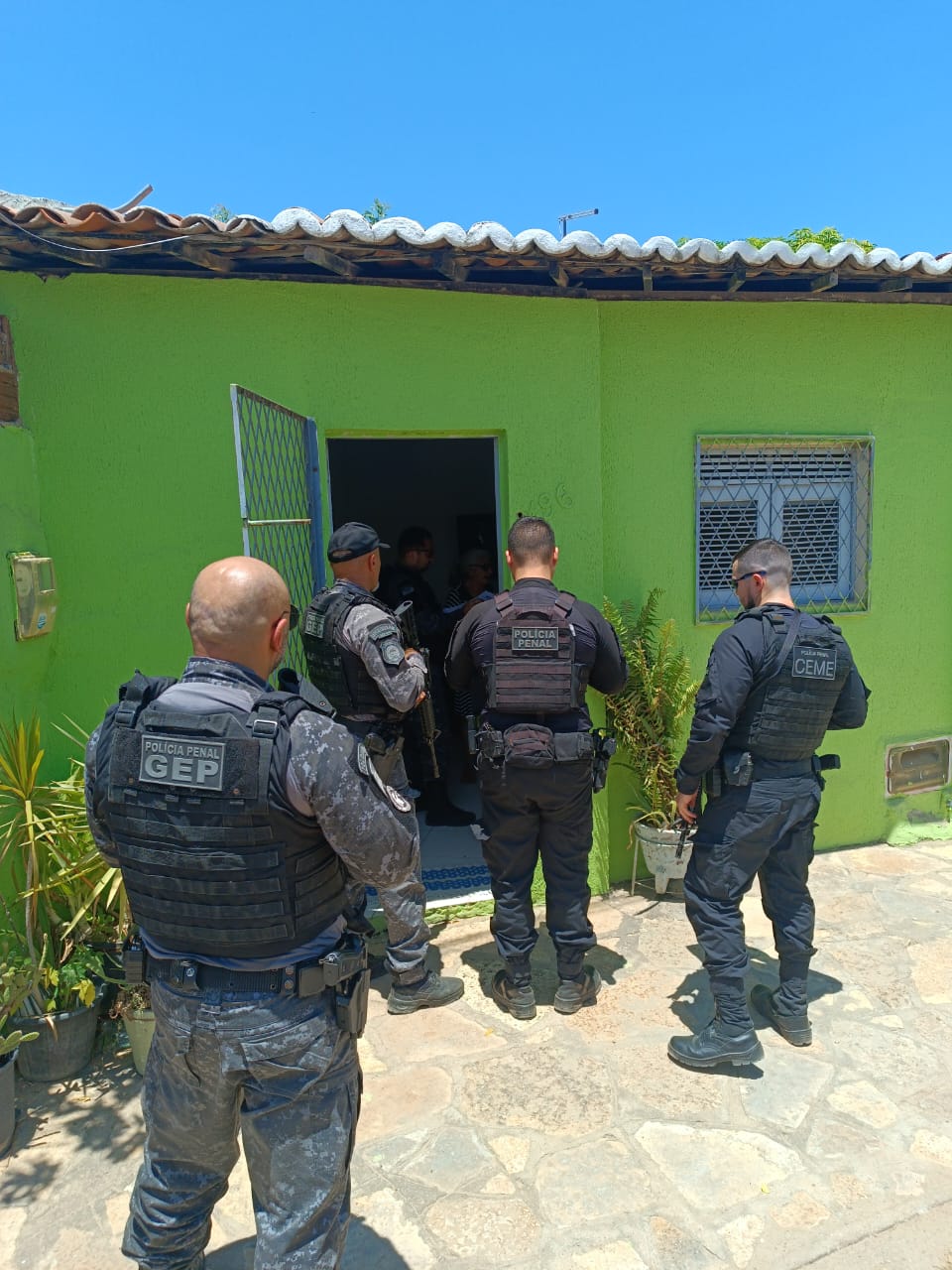 Imagens de quatro policiais militares em frente a uma residência, durante a operação Home Care.