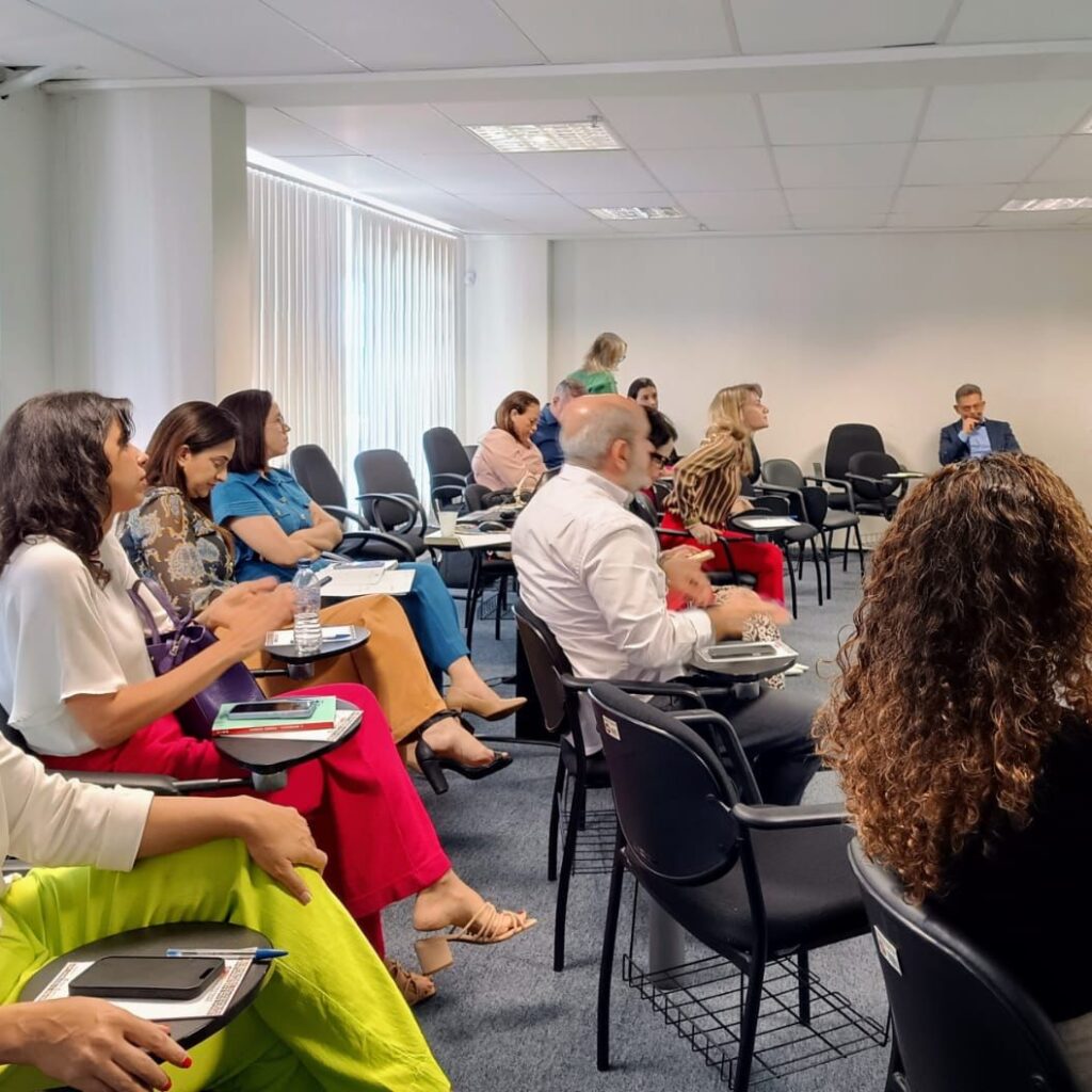 Imagem de várias pessoas sentadas, em uma sala assistindo a uma palestra.