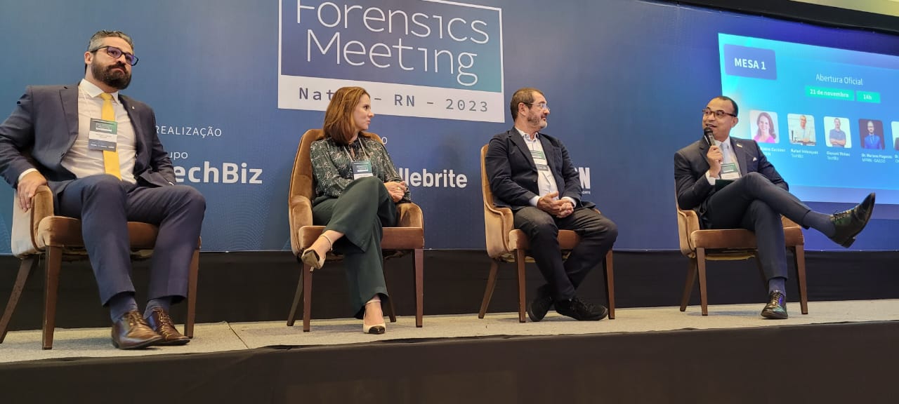 Imagem da procuradora-geral de Justiça Elaine Cardoso ao lado de mais três pessoas, todos sentados,, durante o Forensics Meeting 2023.