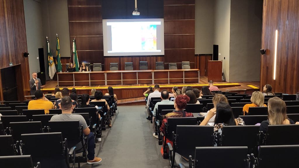 Imagem de um auditório com algumas pessoas sentadas, participando de uma reunião.