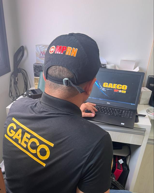 Imagem de um servidor do Gaeco, de costas, sentado, mexendo em um notebook.