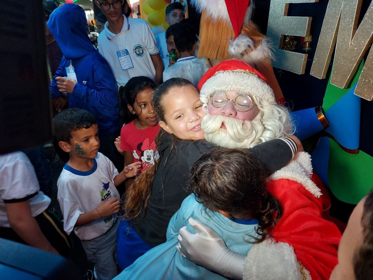 Imagem de papai noel sorrindo abraçando duas crianças.