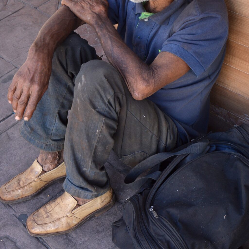Imagem de um homem em situação de rua, sem aparecer o rosto, sentado no chão.