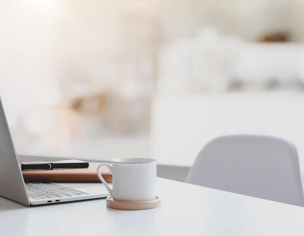 imagem de uma mesa com computador, agenda e caneta e uma cadeira vazia