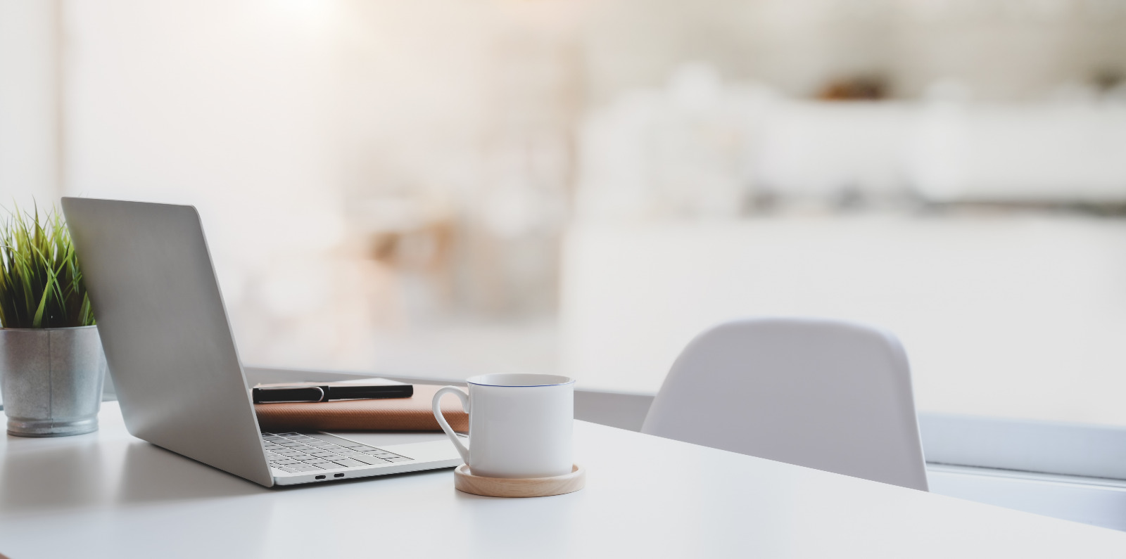 imagem de uma mesa com computador, agenda e caneta e uma cadeira vazia