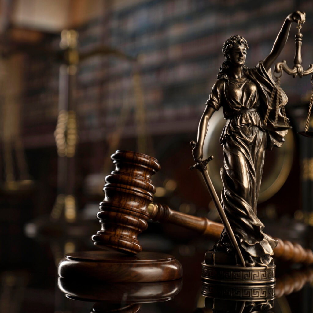 Martelo de madeira da Justiça perto de uma estatua de bronze da Justiça em tamanho pequeno.