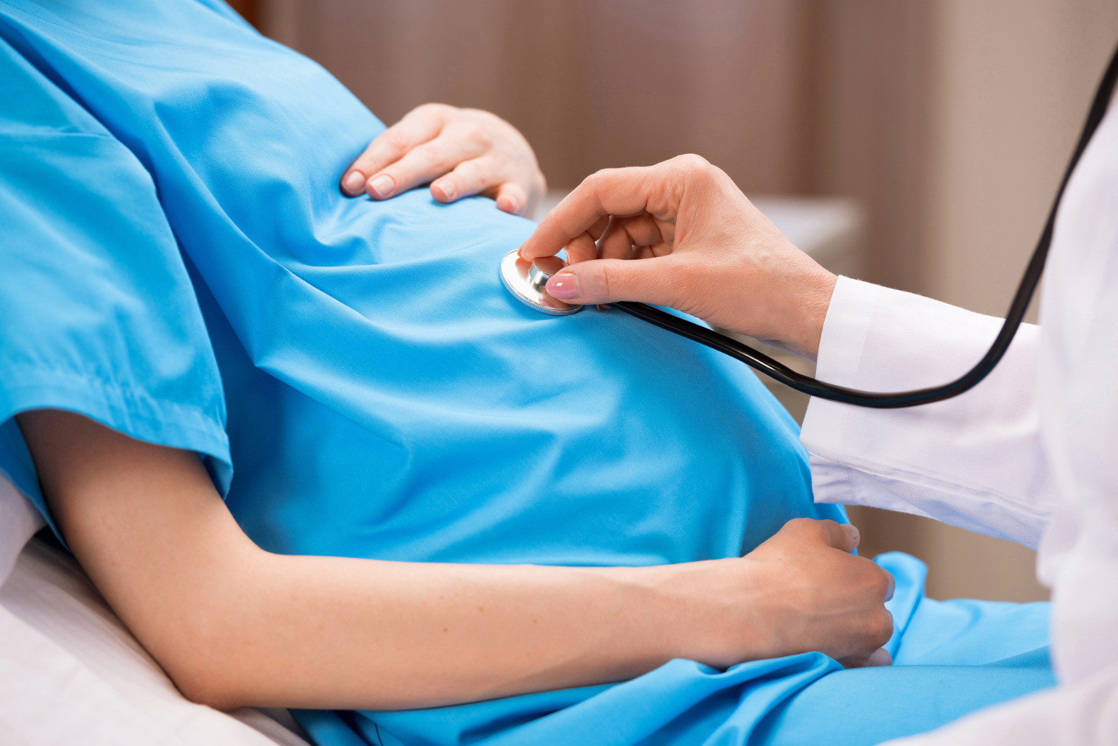 imagem de uma mulher gravida vestindo uma bata azul e uma medico com estetoscopio na barriga dela