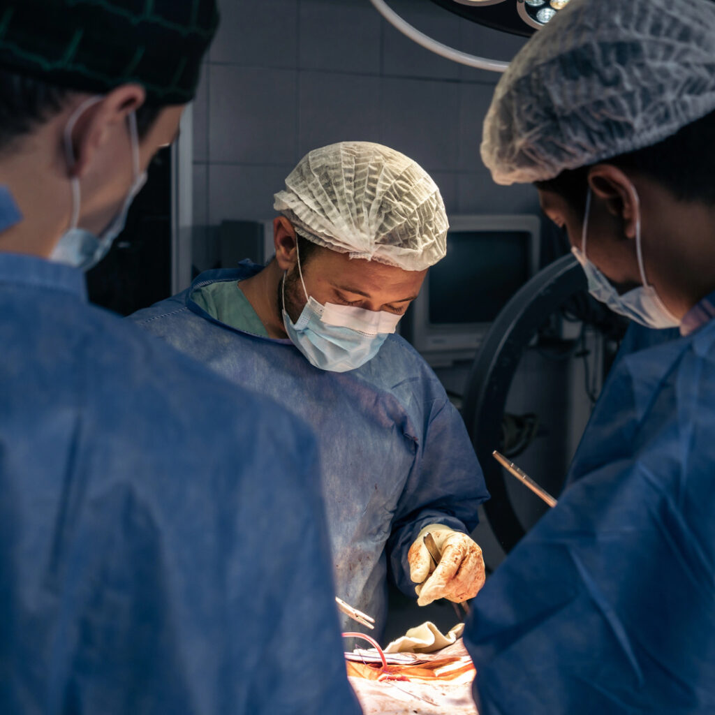 imagem mostram tres profissionais de saude olhando para paciente durante cirurgia