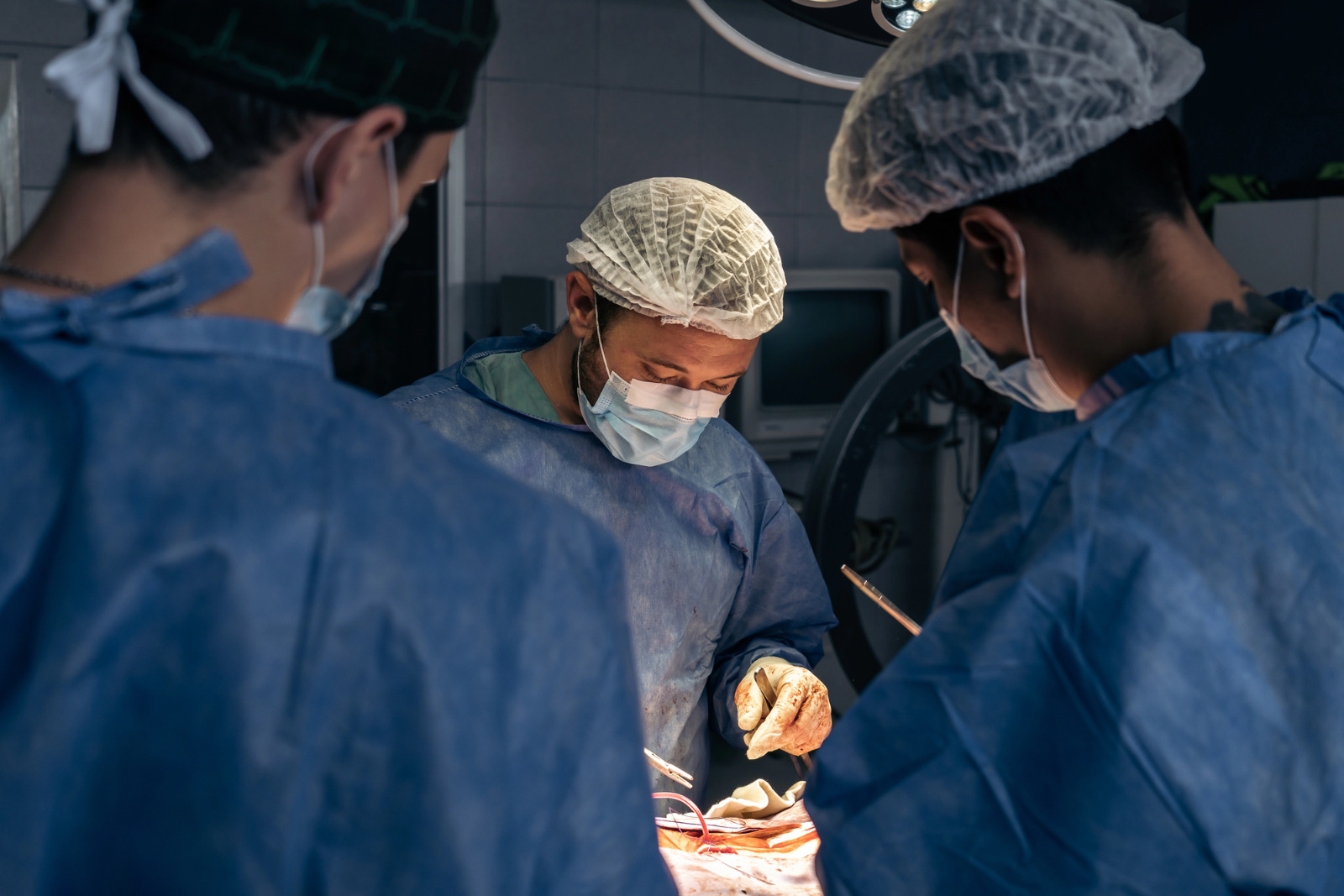 imagem mostram tres profissionais de saude olhando para paciente durante cirurgia
