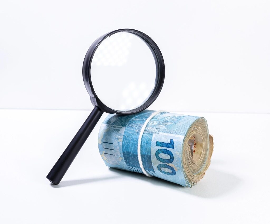 Lupa apoiada em um rolo de dinheiro com notas em real