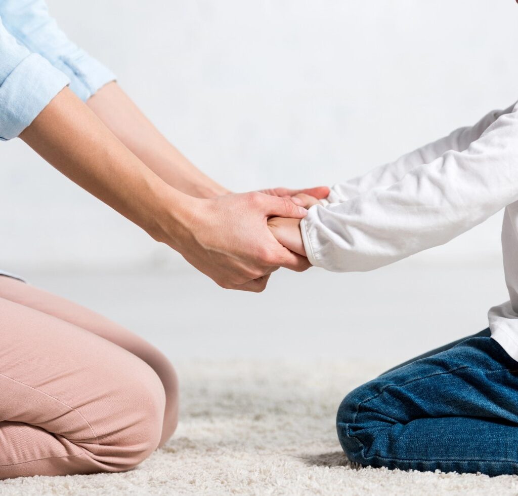 criança e mulher sentadas no chao e de maos dadas