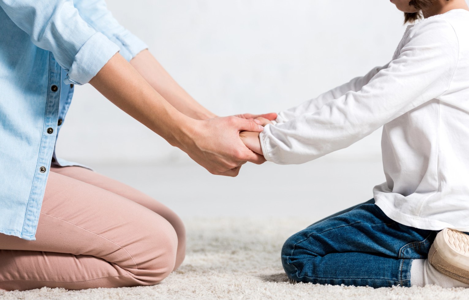 criança e mulher sentadas no chao e de maos dadas
