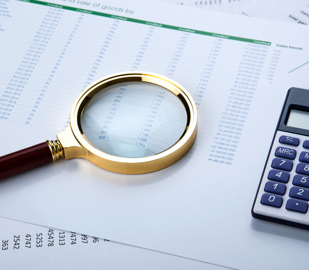 lupa sobre papel com numeros e uma calculadora do lado indicando movimentacao financeira