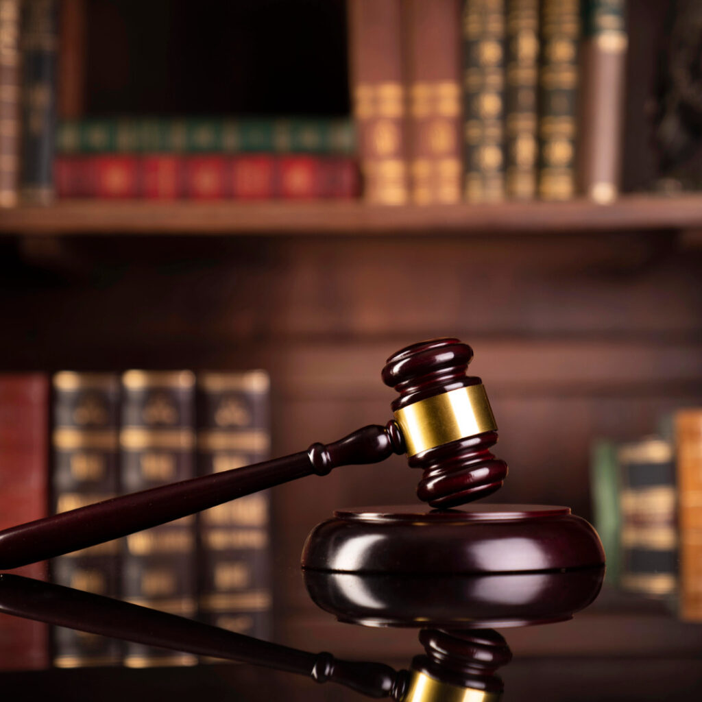 martelo simbolo da justiça em cima de uma mesa, ao fundo de armario com livros antigos