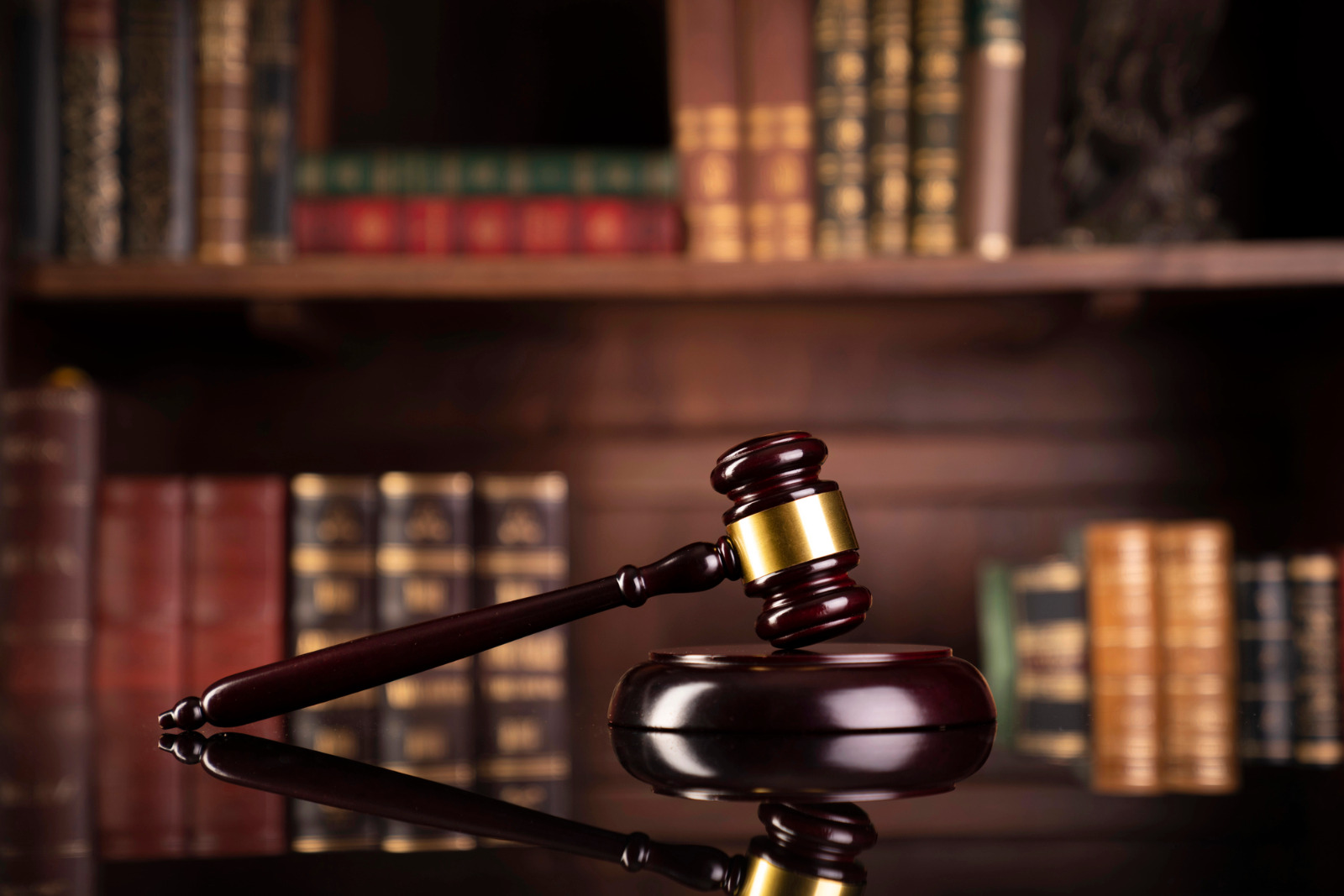 martelo simbolo da justiça em cima de uma mesa, ao fundo de armario com livros antigos