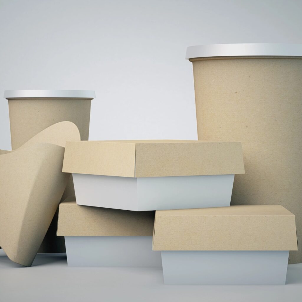 Uma seleção de embalagens para fast-food em papel kraft e branco, incluindo copos com tampa, caixas de hambúrguer e um porta-batatas, dispostos sobre um fundo cinza claro.