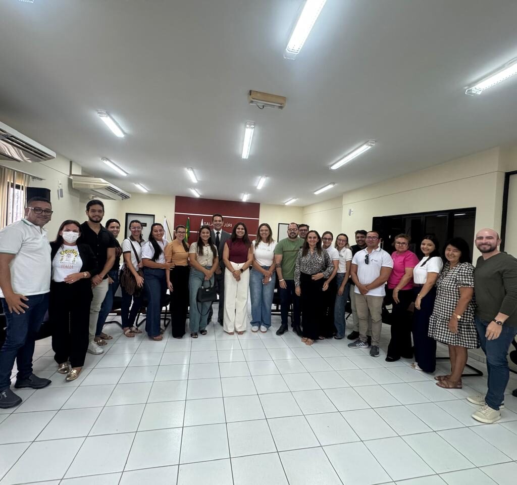 Grupo de pessoas posando sorridentes para uma foto coletiva no centro de uma sala de reuniões ampla e iluminada.