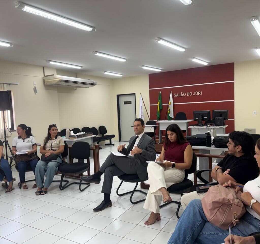 Pessoas sentadas em círculo participando de uma reunião em uma sala com a inscrição "Salão do Júri" ao fundo e o promoto de justica ao centro gesticulando enquanto fala