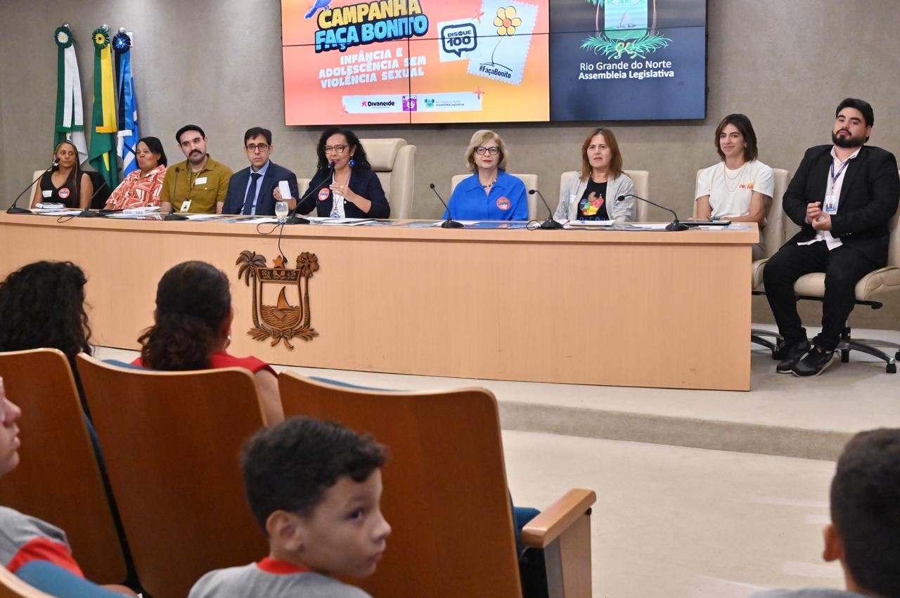 Uma mesa composta por nove autoridades e palestrantes durante um evento na Assembleia Legislativa do Rio Grande do Norte sobre a campanha "Faça Bonito", contra a violência sexual infantil, com público sentado em primeiro plano.