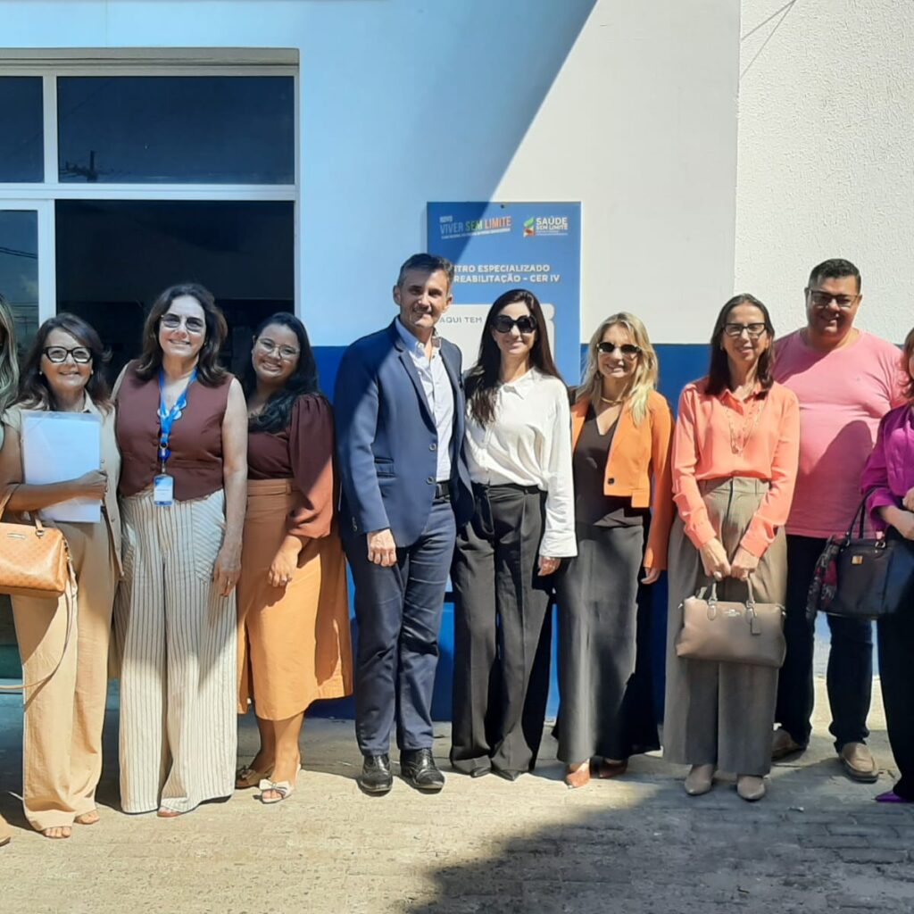 grupo de dez pessoas, vestidas com trajes casuais e formais, sorrindo e posadas lado a lado em frente à entrada de um prédio público