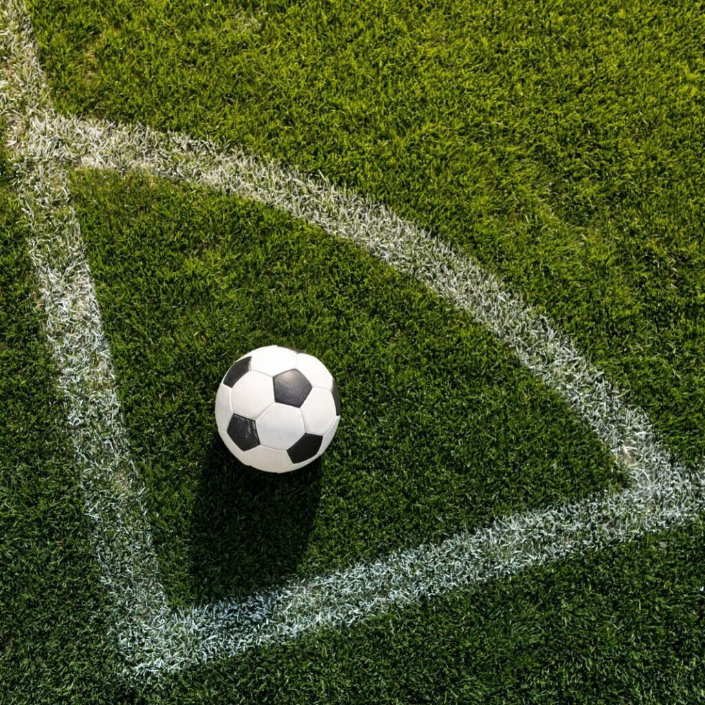 bola de futebol sobre gramado verde posicionada exatamente no local de bater escanteio