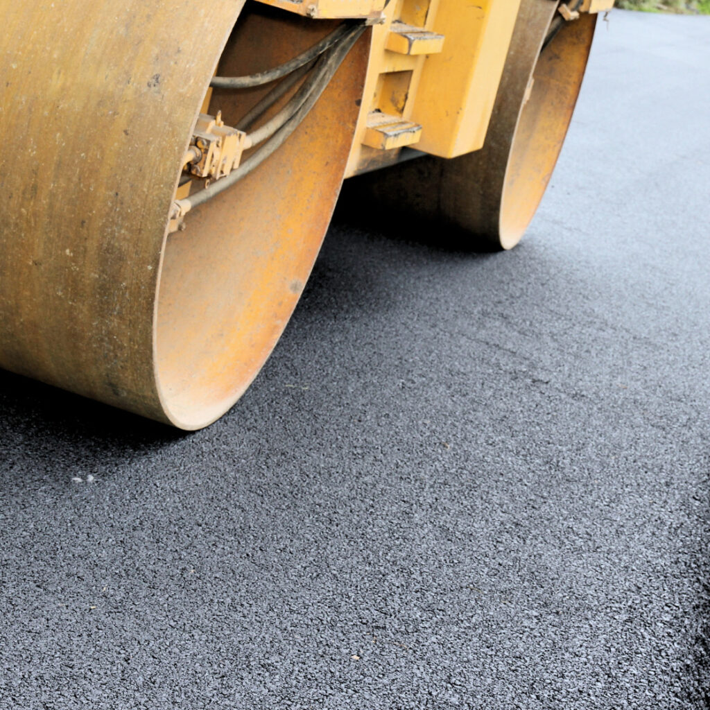 rolo compressor de metal amarelo compacta uma camada de asfalto preto e fresco em uma estrada em construção.