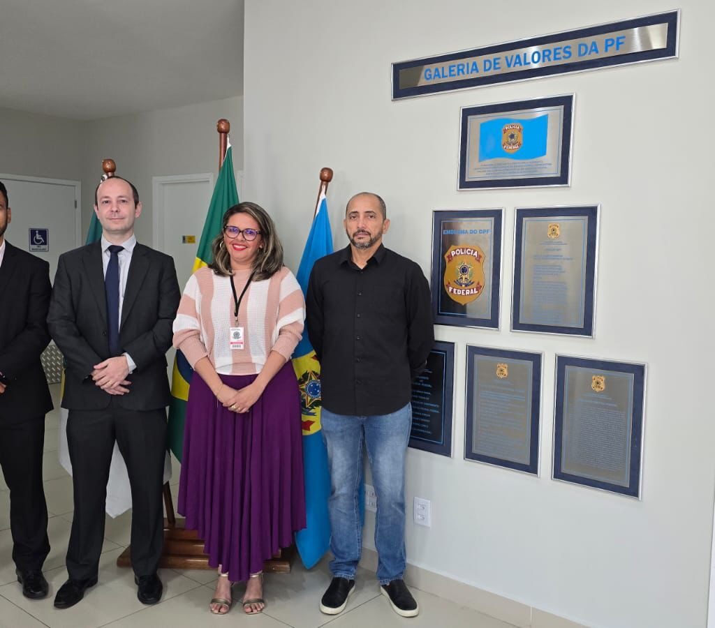 Quatro pessoas — três homens e uma mulher — posam lado a lado sorrindo em um ambiente institucional