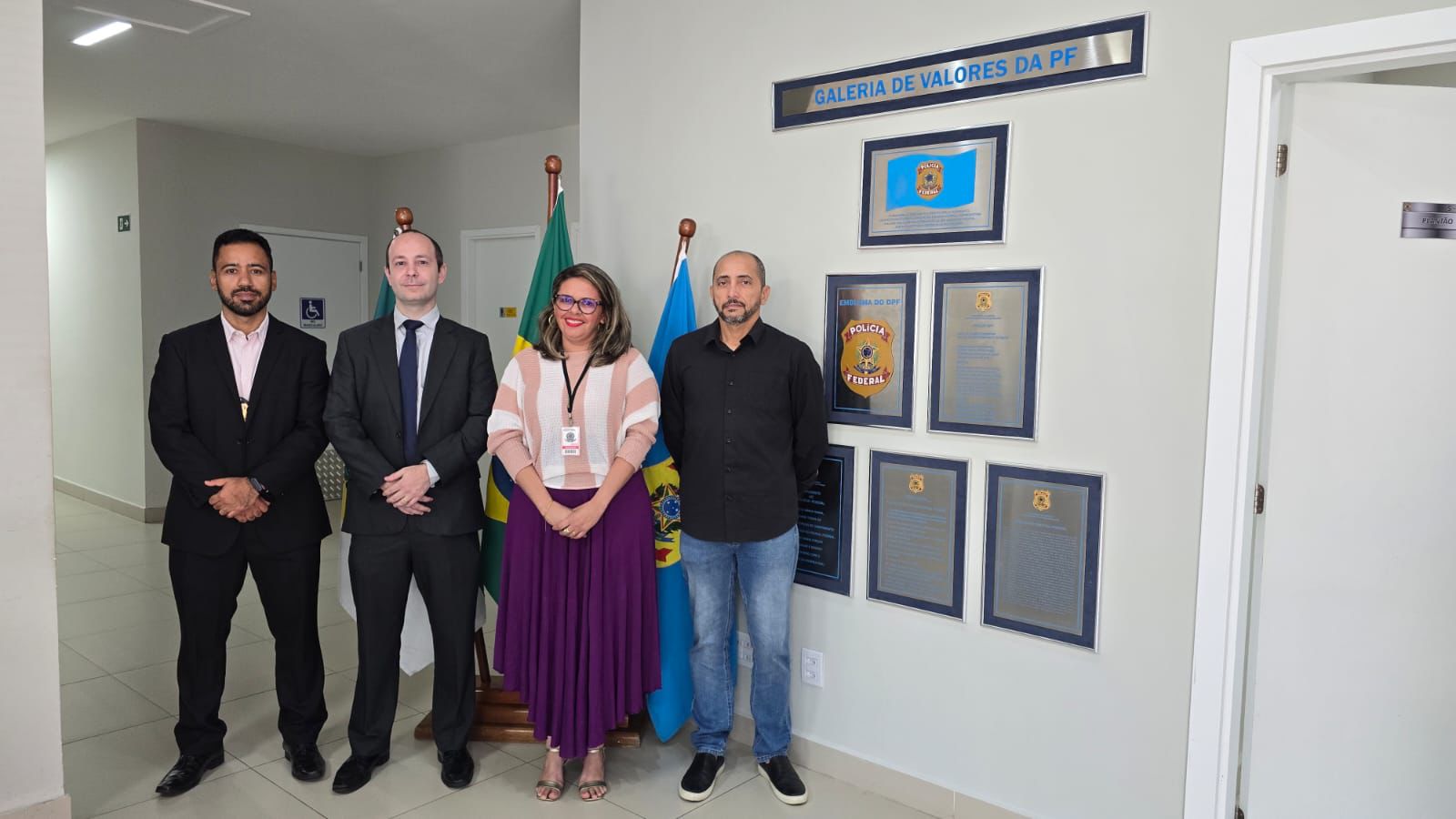 Quatro pessoas — três homens e uma mulher — posam lado a lado sorrindo em um ambiente institucional