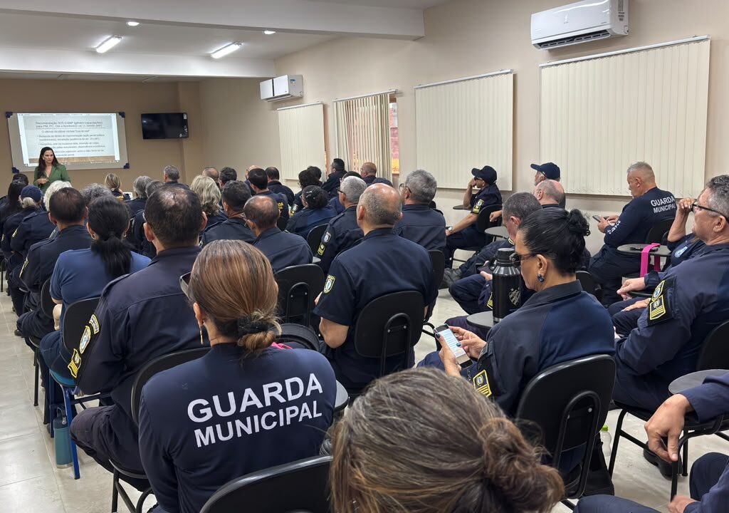Guardas municipais vestindo farda azul sentados num auditório de costas para quem fez a foto