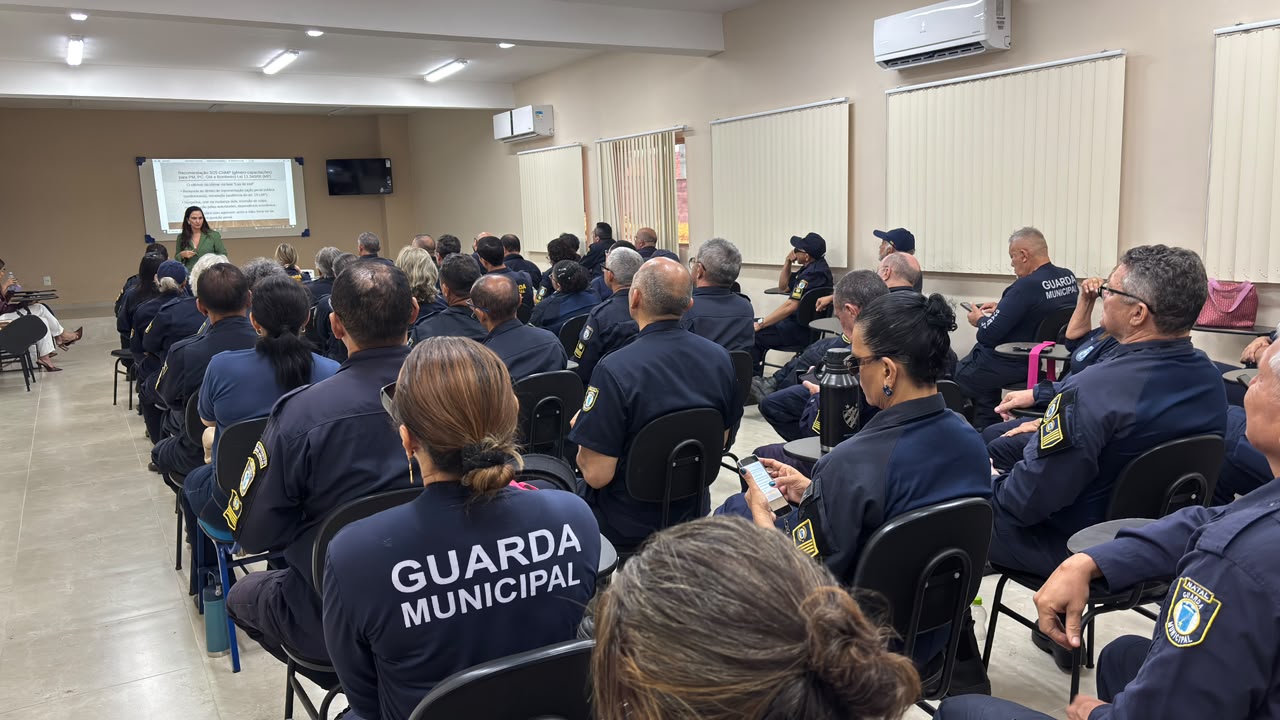Guardas municipais vestindo farda azul sentados num auditório de costas para quem fez a foto