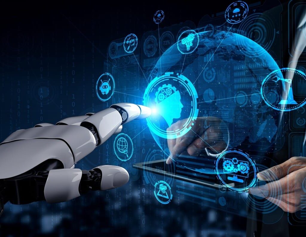 Uma mão robótica branca toca uma interface digital futurista azul cheia de ícones de tecnologia, ao lado das mãos de um homem de terno segurando um tablet