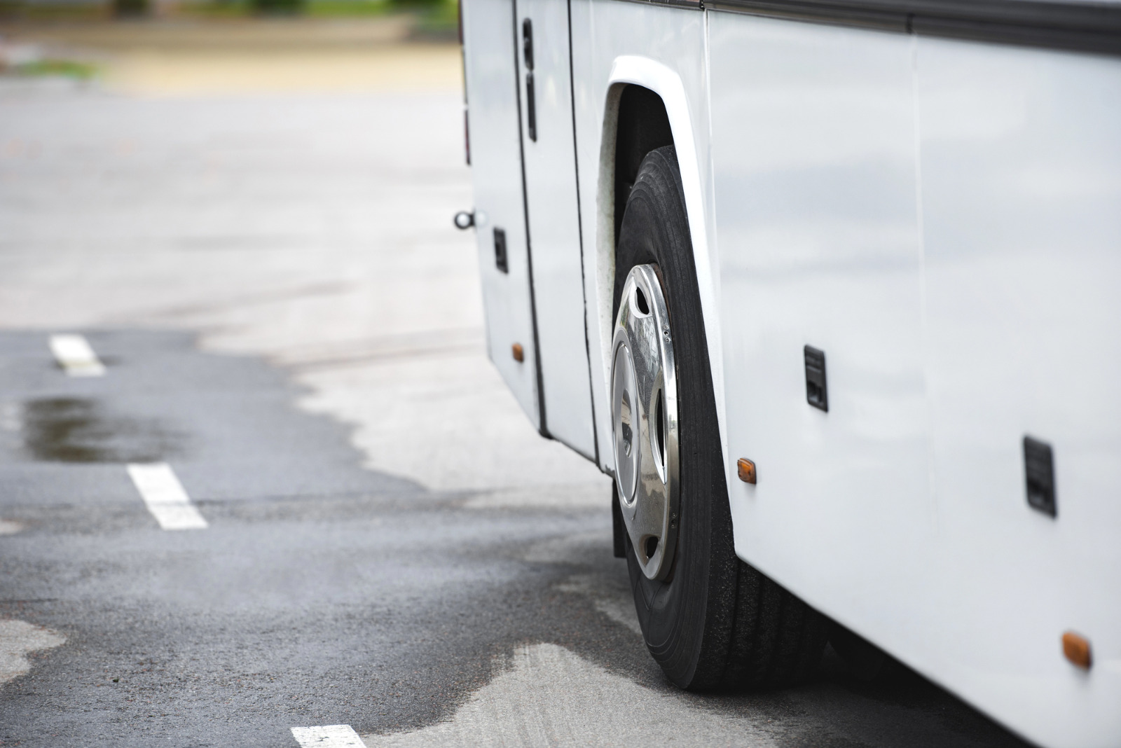 lateral inferior de um ônibus branco estacionado sobre o asfalto molhado, destacando um de seus pneus com calota cromada
