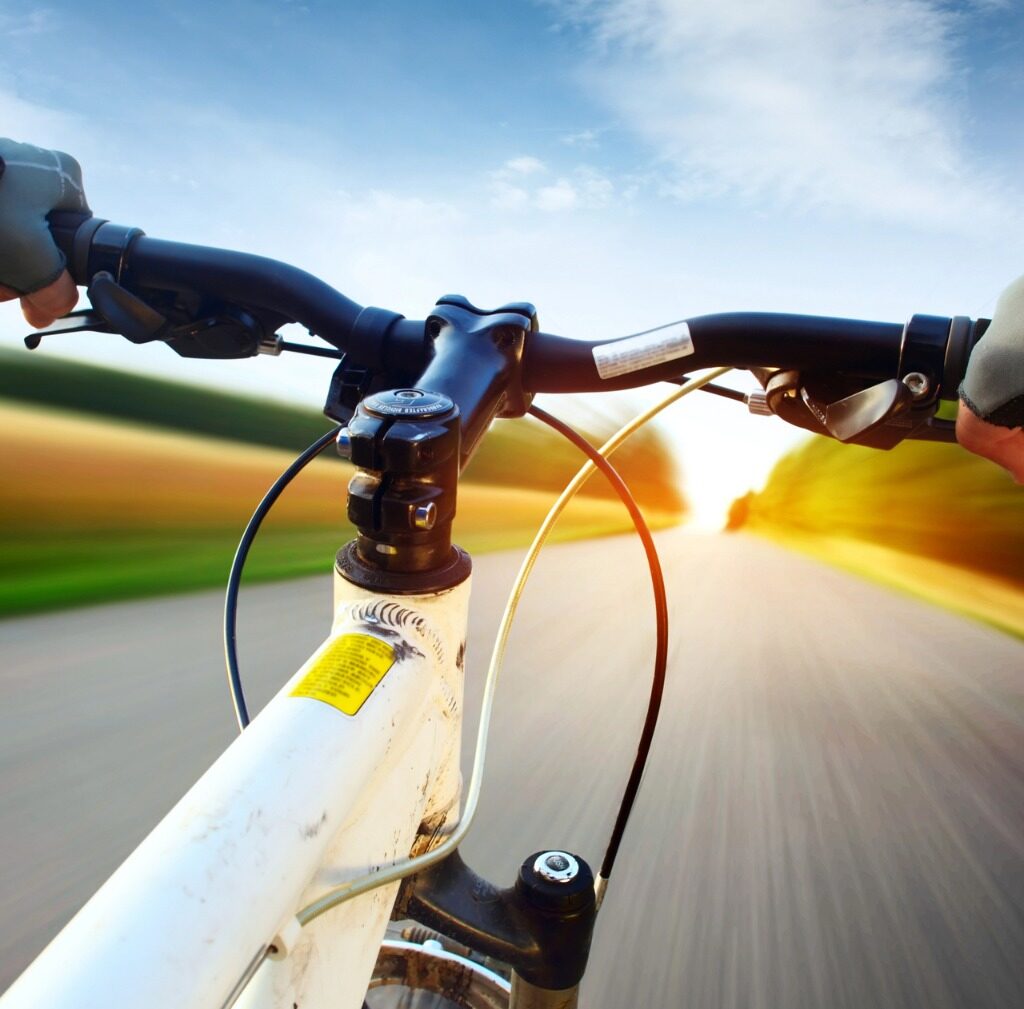 Visão em primeira pessoa de um ciclista segurando o guidão de uma bicicleta enquanto pedalando em uma estrada