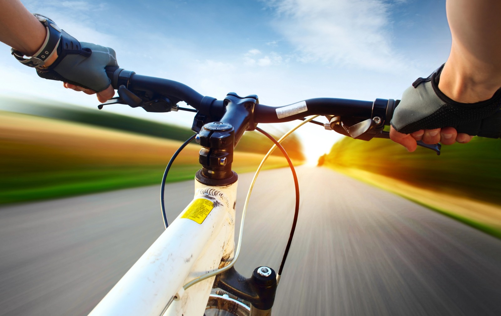 Visão em primeira pessoa de um ciclista segurando o guidão de uma bicicleta enquanto pedalando em uma estrada