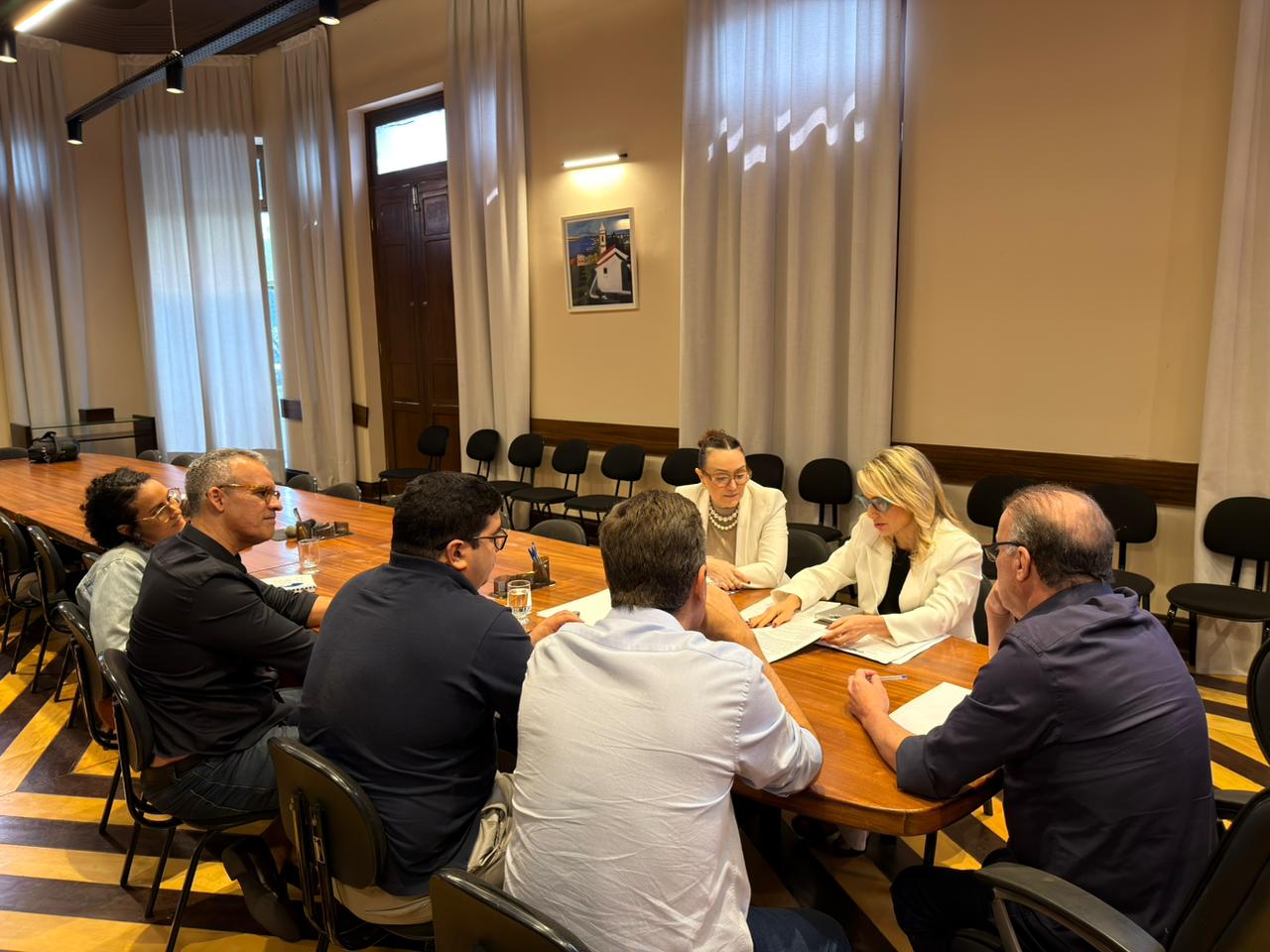 seis pessoas sentadas em mesa de reuniao com o prefeito a ponta e promotoras ao lado