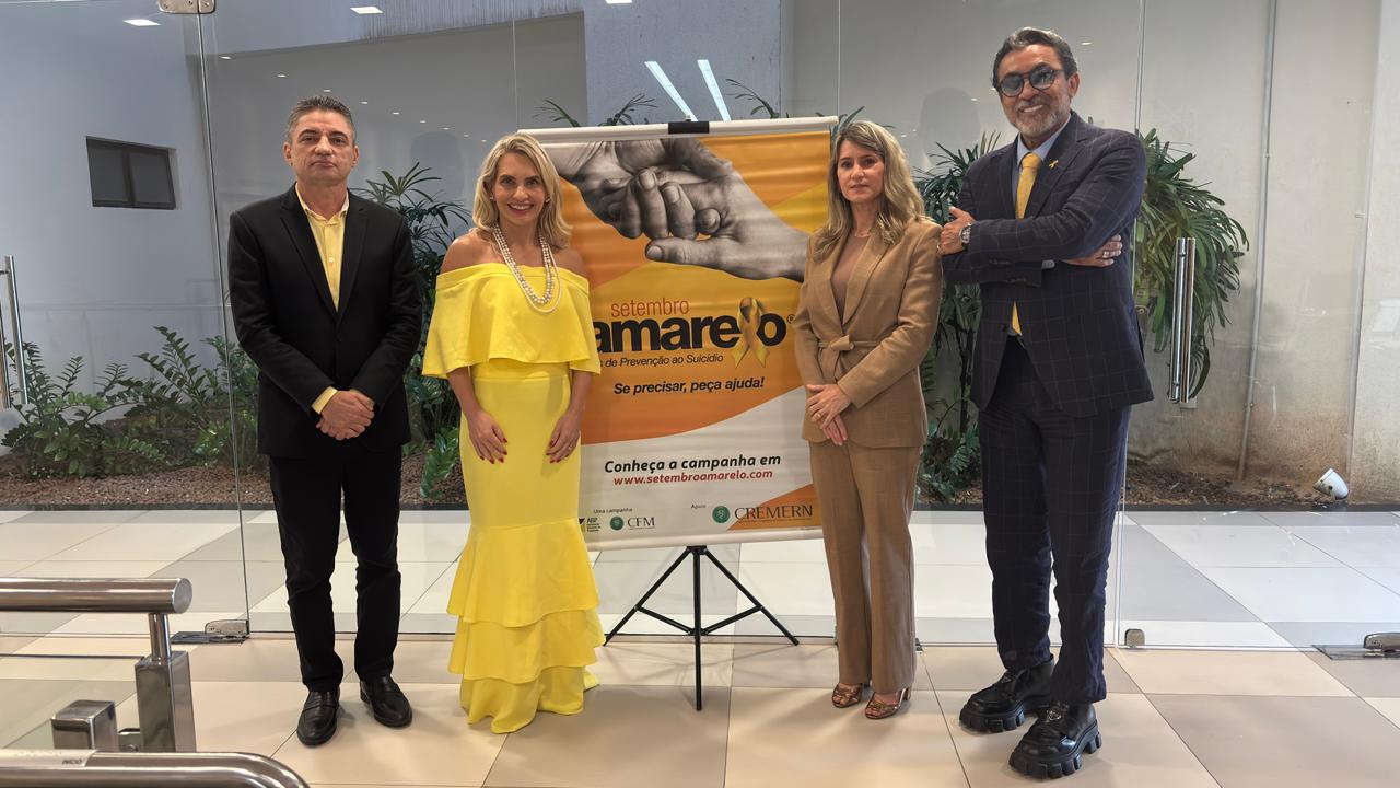Quatro pessoas vestidas formalmente estão lado a lado ao redor de um banner da campanha Setembro Amarelo.
